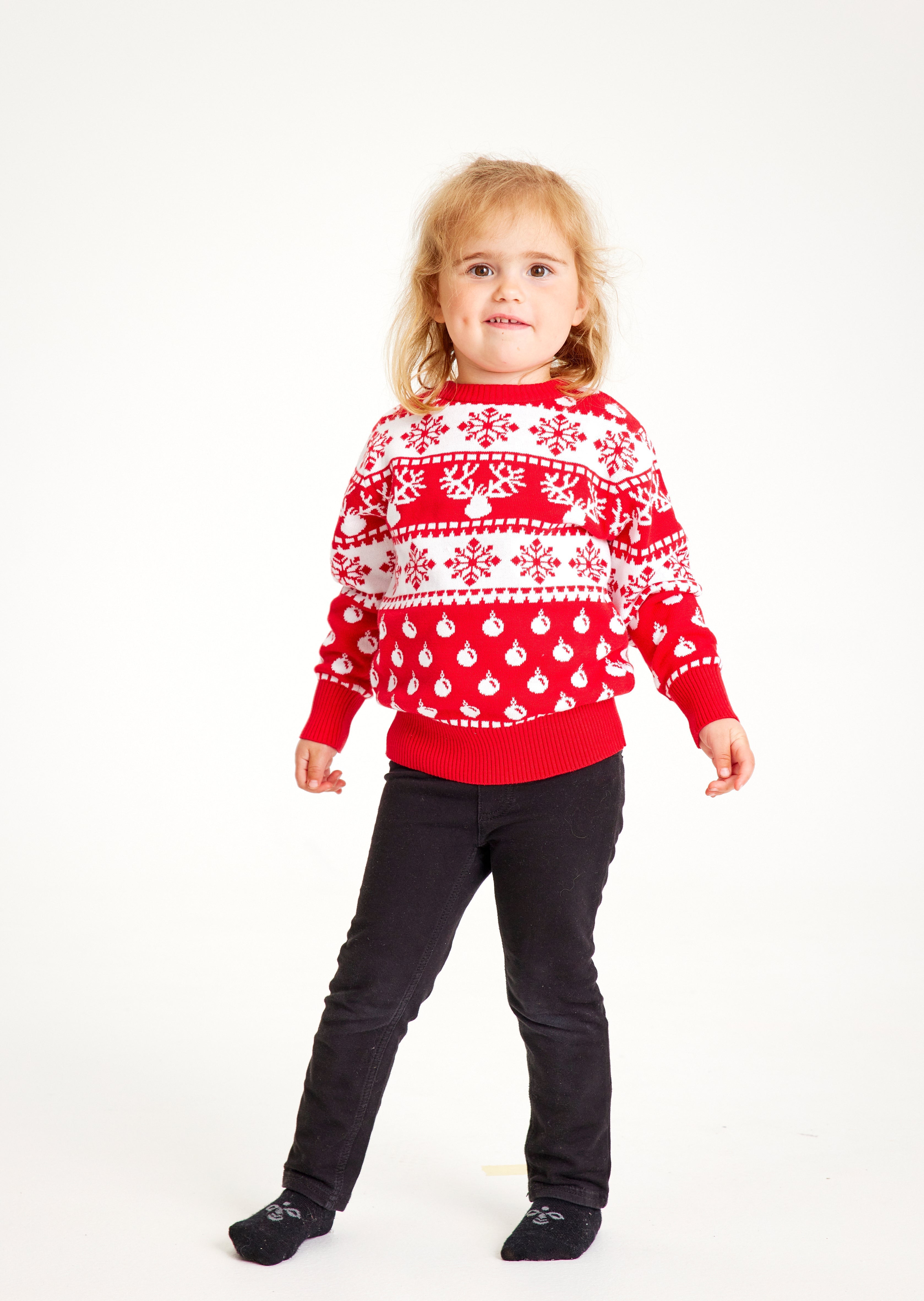 Et barn med rød julegenser med julemønster og reinsdyr.